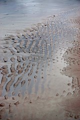 Rippled patterns of water in the red sand on a beach.