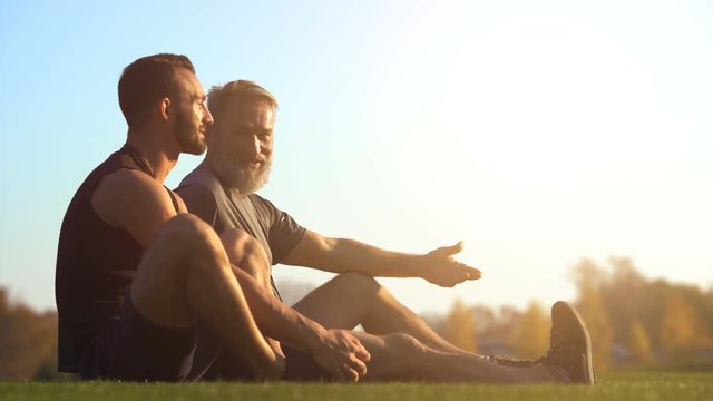 The happy father and a son sitting on the grass and talking