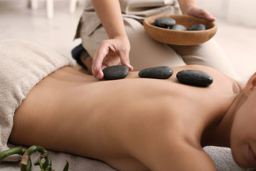 Beautiful young woman getting hot stone massage in spa salon - obrazy, fototapety, plakaty