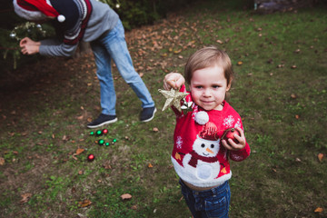Merry Christmas and Happy Holidays. Little girl heps her father decorating the Christmas tree outdoor in the yard of the house before holidays