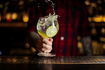 Bartender making splash of a Gin Tonic cocktail decorated with lime slices