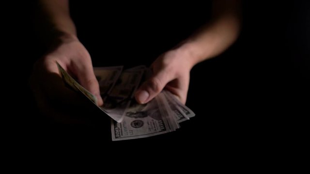 Men's hands count dollars in the dark. The man counts the dollars. The employee received wages in cash. The fee for the work done.He shakes with money. 4k slow motion