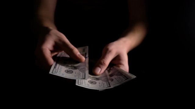 Men's hands count dollars in the dark. The man counts the dollars. The employee received wages in cash. The fee for the work done.He shakes with money. 4k slow motion