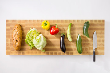 a cutting board and a knife, bread, cabbage, eggplant, green pepper, cucumber