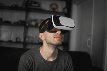 Young bearded man wearing headset of virtual reality in office sitting on a sofa.