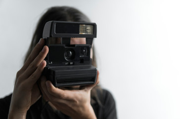Handsome young bearded man with a long hair and in a black shirt holding vintage old-fashioned film camera on a white background and looking in camera viewfinder.