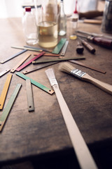 Paint brush, solvents and wood color samples on an old work bench. Focus is on center brush metal sleeve. Shallow depth of focus.