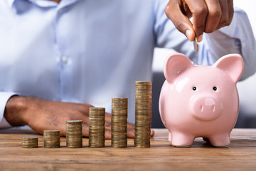 African Man Inserting Coin In Piggybank