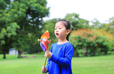 Adorable little Asian kid girl blowing wind turbine in the summer garden.