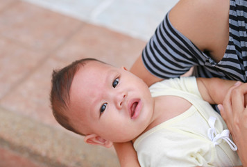 Close-up Asian baby boy lying in hug of mother with looking camera.