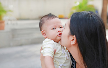 Portrait of Asian mother carrying and kissing her infant baby boy outdoor.