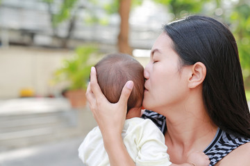 Portrait of Asian mother carrying and kissing her infant baby boy outdoor.