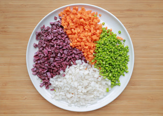 Chopped asparagus, carrot, radish and sweet purple potatoes on white plate against wooden background.