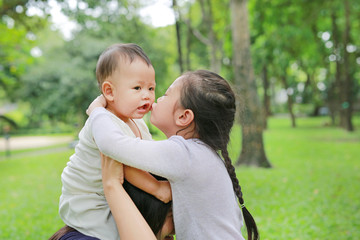 Close up baby boy riding on mom's shoulder with sister kissing in the nature park.