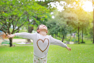 Happy little Asian child girl opened her hands and looking up in the fresh summer garden.