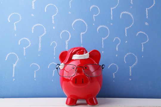 Red piggy bank with glasses in front of a blue chalkboard full of question marks