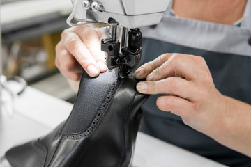 Sewing machine in a leather workshop in action with hands working on a leather details for shoes....
