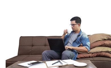 Asian guy drinking coffee while using laptop sitting on sofa working as freelance at home with clipping path for graphic design