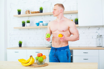 Muscular man with a naked torso in the kitchen with fruit, concept of healthy eating. Athletic way of life.