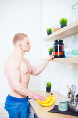Muscular man with a naked torso in the kitchen with a sports nutrition protein and bananas, the concept of a healthy diet. Athletic way of life.