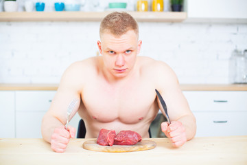 Muscular man with a naked torso in the kitchen with a piece of beef meat, the concept of a healthy diet. Athletic way of life.