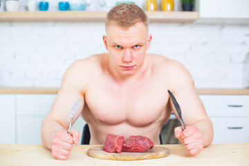 Muscular man with a naked torso in the kitchen with a piece of beef meat, the concept of a healthy diet. Athletic way of life.