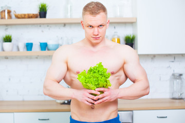 Muscular man with a naked torso in the kitchen with a salad, concept of healthy eating. Athletic way of life.