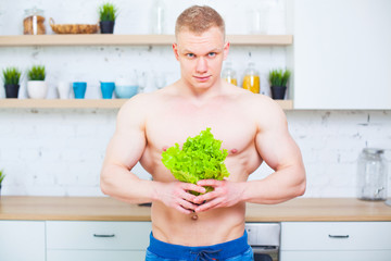 Muscular man with a naked torso in the kitchen with a salad, concept of healthy eating. Athletic way of life.
