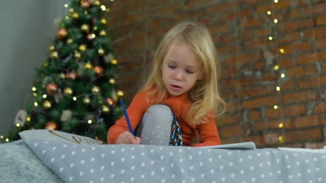 Little Girl Drawing a Picture Near the Christmas Tree