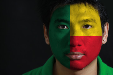 Portrait of a man with the flag of the Benin painted on his face on black background, A horizontal bicolor of yellow and red with a green vertical band.
