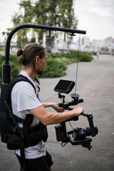 Fototapeta premium Professional videographer holding camera on 3-axis gimbal which mounted on easy rig. Videographer using steadicam. Pro equipment helps to make high quality video without shaking.