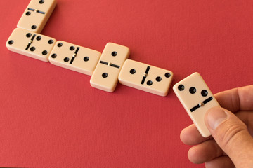 Playing dominoes on a red background . Man's hand with a Domino