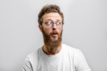 Surprised caucasian man with curly hair and beard stares in amazement aside, dressed in casual...