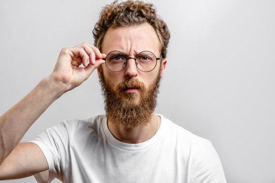 Headshot of serious bearded ners, scientist, with mustache and beard, wears round spectacles, has stylish hairdo, looks confidently.