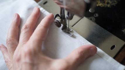 Sewing process. Foot of old vintage sewing machine and hands of elderly woman. Selective focus