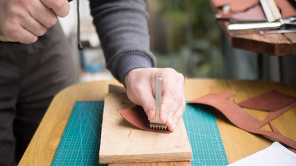 Tanners hands at work with step punch, hammer and leather. Selected focus, close up.