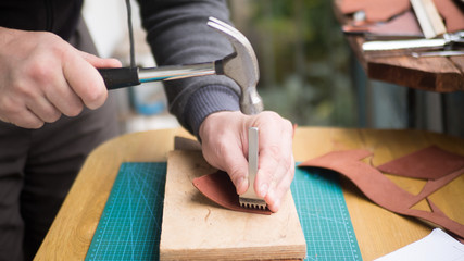 Tanners hands at work with step punch, hammer and leather. Selected focus, close up.