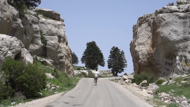 Man running at a natural gate-shaped rock with beautiful trees in the distance