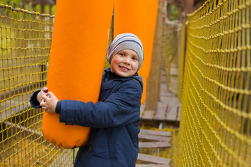 boy plays on the playground, overcomes an obstacle, holds an orange bag and smiles, sport concept