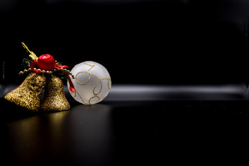 Golden glittered decoration bell and christmas white ball on black.