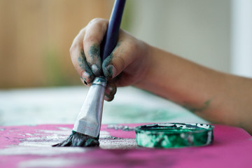 Fototapeta premium small child's hand holding a paint brush to colorful paper 