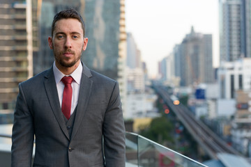 Young handsome Caucasian businessman standing in rooftop at city