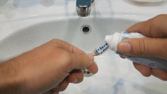 the man squeezes the toothpaste from the tube onto the toothbrush.