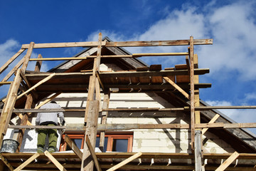 Man working on wooden scaffolding and installing rigid  polystyrene styrofoam plates on residential building facade. House insulation improvement process nd DIY concept.