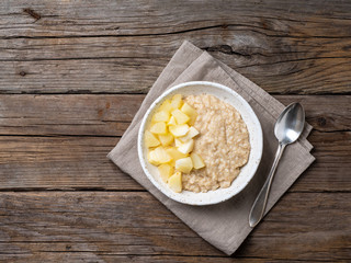 Large bowl of tasty and healthy oatmeal with apple for Breakfast, morning meal. Top view, close up, wooden rustic table