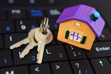 Colorful house model and keys on black laptop keyboard background closeup view. Online house loan, buying or selling real estate on internet or renting new home concept.