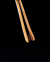 Coffee bean in wooden tweezers on a black background.