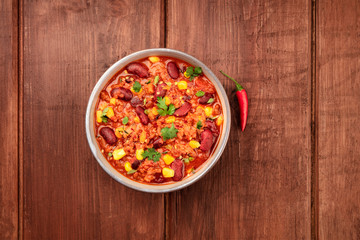 A photo of chili con carne with a chilli pepper, shot from above on a dark rustic wooden background with copy space