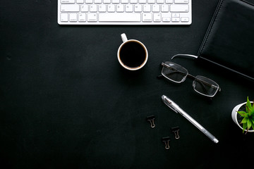 Office desk of chief, director or top manager. Computer keyboard, expensive black notebook, glasses, coffee on black background top view copy space