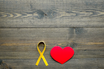 Endometriosis. Gynecological diseases concept. Symbolic yellow ribbon near heart sign on dark wooden background top view copy space